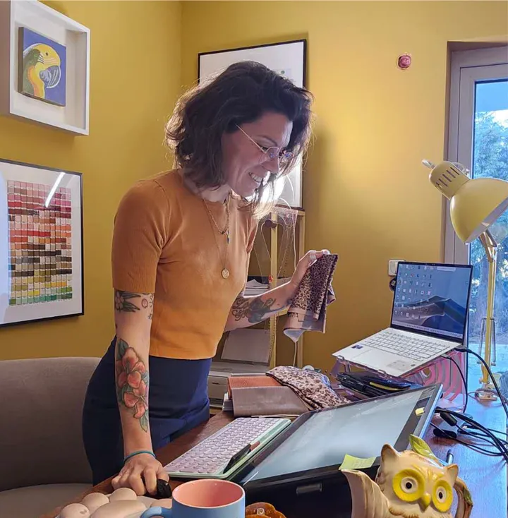 Èlia Barriga Polo in her studio holding fabric swatches beside her work desk